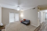 This well-appointed 2-bedroom, 2-bathroom unit in Huffman, TX offers a practical and comfortable single-floor layout. The living room is a welcoming space featuring crown molding, plush carpet, a ceiling fan, and French doors that invite natural light. The galley-style kitchen is efficiently designed with warm wood-toned cabinetry, dark countertops, wood-look flooring, and black appliances, including a full-size refrigerator and dishwasher, with direct access to a utility room. Both bedrooms are comfortably sized, carpeted, and equipped with ceiling fans and windows with blinds. The primary bedroom benefits from a dedicated walk-in closet with wire shelving spanning three walls, providing generous storage. The two bathrooms mirror each other in style, each featuring wood-look flooring, warm wood cabinetry, and a shower-tub combination. One bathroom includes an overhead cabinet above the toilet, while the other features a long vanity with an extended countertop and large mirror. A separate utility room adds further practicality to this thoughtfully arranged home.