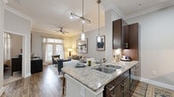 Located at 3838 N Braeswood Blvd in Houston, TX, this thoughtfully designed one-bedroom, one-bathroom residence offers a cohesive open-concept layout that maximizes every square foot. The kitchen serves as a central focal point, featuring granite countertops, rich dark-wood cabinetry, stainless steel appliances, a double-basin sink, and pendant lighting that illuminates the peninsula. Track lighting and crown molding add refined detail to the ceilings throughout. The combined dining and living area flows seamlessly from the kitchen, bathed in natural light from floor-to-ceiling windows and a glass door that opens to an outdoor balcony. Wood-style flooring, a ceiling fan, and neutral tones create a warm, inviting ambiance. The bedroom offers a carpeted, restful retreat with ample space, accompanied by two well-organized closets featuring built-in wire shelving systems for efficient storage. The bathroom is finished with granite countertops, warm wood vanity cabinetry, tile flooring, and a full soaking tub with tiled surround. Additional conveniences include a dedicated laundry area and utility room, making this a fully functional and elegantly appointed home.