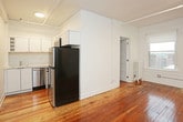 This single-floor unit is characterized by rich, warm hardwood floors that run throughout the main living areas, complementing the clean white walls and creating a bright, inviting atmosphere. The open layout connects the kitchen and living space seamlessly, with natural light flowing in through multiple windows that offer views of the surrounding urban streetscape.

The kitchen is thoughtfully appointed with white cabinetry, stone countertops, and a full suite of stainless steel appliances, including a gas range with an over-the-range microwave, dishwasher, and a black refrigerator. Track lighting overhead keeps the space well-lit and functional.

The living area is generously proportioned, featuring tall ceilings with exposed track lighting rails and a classic cast-iron radiator beneath a large window. A separate bedroom area also benefits from natural light via double windows, with paneled white doors adding a traditional touch.

The bathroom is finished with floor-to-ceiling white subway tile surrounding a soaking tub and shower combination, a wall-mounted sink with a modern faucet, a mirrored medicine cabinet, and marble-style tile flooring. Adjacent to the bathroom is a walk-in closet outfitted with built-in wire shelving, providing practical and organized storage throughout the unit.