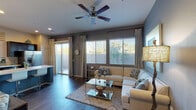 This single-floor residence offers a thoughtfully designed layout with contemporary finishes and a cohesive color palette of cool grays, teal accents, and warm wood tones. The living room is a comfortable, well-lit space featuring dark hardwood-style flooring, bold gray accent walls, large windows with plantation shutters and elegant drape panels, and a ceiling fan overhead. A sliding glass door connects the living area to an outdoor patio, allowing natural light to fill the room. The kitchen is a standout feature, showcasing rich dark cabinetry, light quartz countertops, a full suite of stainless steel appliances including a range, built-in microwave, dishwasher, and refrigerator, and a teal-accented island with bar seating — ideal for casual dining or entertaining. The primary bedroom is serene and spacious, with a teal feature wall, wood-style flooring, and generous natural light from multiple windows. Its en-suite bathroom includes a wide vanity with ample counter space and direct access to a walk-in closet. The secondary bedroom is bright and well-proportioned, featuring neutral tones and a rustic wood dresser. A second full bathroom serves the remaining rooms, complete with a vanity, tub/shower combination, and a tall window for natural ventilation.