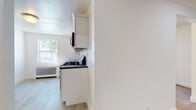 Located at 264 Faller in New Milford, NJ, this single-floor unit offers a clean, freshly updated interior designed for comfortable everyday living. The kitchen is a standout feature, showcasing white shaker-style cabinetry with brushed nickel hardware, dark countertops, and a classic white subway tile backsplash. Stainless steel appliances include a gas range, dishwasher, and over-the-range microwave, all complemented by light wood-look flooring that adds warmth to the space. Natural light filters in through a window, enhancing the bright, airy feel of the kitchen area. The living and bedroom spaces feature neutral wall-to-wall carpeting, crisp white walls, and recessed lighting, creating a comfortable and versatile environment. Windows in each room provide views of the surrounding greenery, allowing natural light to flow throughout. Each room is equipped with a wall-mounted air conditioning unit alongside a radiator cover, ensuring year-round comfort. The bathroom is elegantly appointed with large-format marble-look tile flooring, a white vanity, and a tub-shower combination enclosed by sliding glass doors, all finished in a bright, clean aesthetic that ties the space together cohesively.