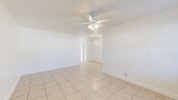 Located at 1860 SW 68th Ave in Miramar, FL, this 1-bedroom, 1-bathroom residence offers a compact and efficiently designed single-floor layout. Light-colored ceramic tile flooring runs consistently throughout the entire unit, creating a cohesive and easy-to-maintain interior. The combined living and dining area serves as the central gathering space, featuring a ceiling fan with light fixture, a wall-mounted A/C unit, and a window that brings in natural light. A modern ring-style pendant chandelier distinguishes the dining area and adds a contemporary touch to the otherwise clean, minimalist aesthetic. The kitchen is bright and functional, equipped with white cabinetry, a smooth-top electric range, over-the-range microwave, refrigerator, and a window with blinds overlooking the outdoors. A hallway connects the living areas to the private spaces and is accented by a second ring pendant light fixture. The spacious bedroom includes a ceiling fan, a wall A/C unit, a window with natural light, and a closet with double panel doors. The bathroom features full-height beige tile surround on the tub/shower combo and a small window for ventilation. Throughout the unit, bright white walls and natural light contribute to an open and airy atmosphere.
