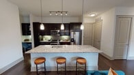 Located along Bluffs Lane in Grapevine, Texas, this single-story residence offers a thoughtfully designed open-concept layout with contemporary finishes throughout. The kitchen serves as a focal point of the living space, featuring rich dark cabinetry, a green subway tile backsplash, stainless steel appliances, and a generous granite-topped island with an undermount sink. Pendant lighting hangs above the island, which accommodates bar seating for casual dining. Track lighting complements the kitchen's functional design, while dark hardwood flooring extends through the main living areas, adding warmth and continuity.

The living room is bathed in natural light through floor-to-ceiling windows and a glass-paneled door that opens to an outdoor area. The space features neutral wall tones and a ceiling fan, creating a comfortable and inviting atmosphere.

The bedrooms each offer plush carpeting, ceiling fans, and windows that allow natural light to filter in. Accent walls in bold tones provide visual character to each room.

The bathroom is finished with a glass-enclosed walk-in shower, dark cabinetry with ample storage, a sleek vanity, and light tile flooring, presenting a clean and functional design aesthetic throughout.