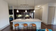Located along Bluffs Lane in Grapevine, Texas, this single-story residence offers a thoughtfully designed open-concept layout with contemporary finishes throughout. The kitchen serves as a focal point of the living space, featuring rich dark cabinetry, a green subway tile backsplash, stainless steel appliances, and a generous granite-topped island with an undermount sink. Pendant lighting hangs above the island, which accommodates bar seating for casual dining. Track lighting complements the kitchen's functional design, while dark hardwood flooring extends through the main living areas, adding warmth and continuity.

The living room is bathed in natural light through floor-to-ceiling windows and a glass-paneled door that opens to an outdoor area. The space features neutral wall tones and a ceiling fan, creating a comfortable and inviting atmosphere.

The bedrooms each offer plush carpeting, ceiling fans, and windows that allow natural light to filter in. Accent walls in bold tones provide visual character to each room.

The bathroom is finished with a glass-enclosed walk-in shower, dark cabinetry with ample storage, a sleek vanity, and light tile flooring, presenting a clean and functional design aesthetic throughout.