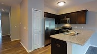 This two-floor residence is designed with a focus on modern aesthetics and practical functionality. The kitchen stands out as a central highlight, showcasing rich dark cabinetry that extends to the upper walls, providing ample storage throughout. Granite countertops in a light speckled finish offer a striking contrast against the dark cabinetry, while a peninsula-style counter adds additional workspace and a casual dining option. The kitchen is fully equipped with a suite of stainless steel appliances, including a French door refrigerator with an in-door water and ice dispenser, a stainless steel range with an electric cooktop, and an over-the-range microwave. Warm hardwood flooring flows throughout, complementing the overall color palette and adding a sense of continuity and warmth to the space. Neutral gray walls provide a clean, versatile backdrop that adapts well to a variety of interior styles. A flush-mount ceiling light fixture provides consistent overhead illumination. A paneled interior door adjacent to the refrigerator leads to additional storage or utility space, enhancing the home's practicality. Spanning two floors, this residence offers generous separation of living and private spaces, making it a well-rounded and thoughtfully designed home.