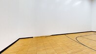 Located at 75 Charolais Blvd in Brampton, Ontario, this indoor basketball court offers a well-appointed recreational space designed for active use. The court features a classic hardwood-style floor finished in a warm natural tone, with clearly marked black court lines including a half-court arc, key markings, and center indicators — providing a proper layout for gameplay and practice.

A wall-mounted basketball hoop with a red backboard and rim is affixed to one end wall, ready for use. The surrounding walls are finished in clean white, lending a bright, open feel to the interior. Overhead, a series of recessed skylight-style flush panel lights illuminate the entire court evenly, ensuring excellent visibility throughout.

A set of interior windows positioned high on one wall allow for observation from an adjacent area, adding a functional supervisory or spectator element to the space. A single access door is located along the same wall, providing entry to the court. Black rubber base trim runs along the perimeter where walls meet the floor, giving the space a tidy, finished appearance.

Overall, this self-contained indoor court is a practical and functional athletic amenity, well-suited for basketball, multi-sport training, or recreational activities.