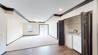 This single-floor residence combines functional design with refined finishing details throughout its well-organized layout. The living area is a generously sized, light-filled space featuring plush neutral carpeting and crisp white walls accented by bold dark crown molding and matching baseboards, which lend a polished contrast to the overall aesthetic. A sliding glass door opens to an outdoor view, allowing natural light to fill the room, while a secondary window further brightens the space.

The kitchen is well-appointed with dark espresso cabinetry extending to the ceiling for ample storage, granite-style countertops, and a full suite of stainless steel appliances including a refrigerator, range, dishwasher, and microwave. Warm hardwood-style flooring runs throughout this area. Conveniently adjacent, an in-unit washer and dryer are accessible directly from the kitchen.

The bedrooms offer soft carpeting, natural light from windows, and generous closet space, including a walk-in closet fitted with multi-tier wire shelving. The bathrooms are cleanly finished with dark vanity cabinetry, a white countertop, classic black-and-white mosaic tile flooring, a tub-shower combination, and a separate walk-in shower stall with brushed nickel fixtures.