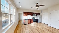 This single-floor unit offers a well-designed, open-concept layout with light hardwood flooring that runs seamlessly throughout the space. The kitchen and living area share an open, airy floor plan, creating a cohesive and functional living environment. Recessed lighting and a ceiling fan with a built-in light fixture provide ample illumination while contributing to the room's modern aesthetic.

The kitchen is equipped with rich, dark cherry wood cabinetry paired with a white subway tile backsplash and light-toned countertops, creating a striking contrast. A full suite of stainless steel appliances—including a refrigerator, electric range, over-the-range microwave, and dishwasher—rounds out the kitchen's practical offerings.

The living area benefits from a large multi-pane window that frames neighborhood views and draws in generous natural light. A ceiling fan overhead enhances comfort year-round.

The bedroom is a bright, spacious retreat with its own multi-pane window offering outdoor views. It features direct access to a dedicated walk-in closet with built-in shelving and an en-suite bathroom outfitted with marble-style tile flooring, a vanity, toilet, and a glass-door walk-in shower. Additional closet storage is also available in the main living area.
