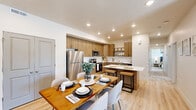 This well-appointed single-floor residence offers a thoughtfully designed open-concept layout with modern finishes throughout. The kitchen serves as a central highlight, featuring warm wood-toned cabinetry, stainless steel appliances including a refrigerator, microwave, and range, a classic white subway tile backsplash, and a sleek white-topped island with bar seating. Light wood-style flooring flows seamlessly from the kitchen into the adjacent dining area, which comfortably accommodates a full dining table and chairs. The living room is bright and airy, filled with natural light through large windows and a set of glass French doors that open to an outdoor area. A ceiling fan adds comfort, and the open layout creates an inviting, relaxed atmosphere. The primary bedroom is a serene retreat, complete with a ceiling fan, access to a walk-in closet, and clean white walls that enhance the sense of openness. A secondary bedroom is configured for flexible use, ideal for children or guests, with light wood flooring and good natural light. A dedicated home office provides a quiet workspace with a window that allows natural light. The in-unit laundry room houses a full-sized top-load washer and dryer with built-in shelving above. The overall design balances contemporary style with functional living across every space.