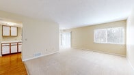 Located at 700 Shadybrook Dr in Akron, Ohio, this two-floor home offers a straightforward, functional layout with consistent finishes across both levels. The main floor features a spacious living area with neutral-toned carpet, warm beige walls, and a textured ceiling. Large sliding glass doors dressed with vertical blinds, along with a side window, allow abundant natural light to fill the room. A pendant light fixture marks the transition toward the dining area. The kitchen is laid out in a galley configuration, featuring white cabinetry with wood trim accents, white appliances including a refrigerator, dishwasher, and electric range, light-toned countertops, and warm hardwood-style flooring. An entry-level room with matching hardwood-style flooring leads to the staircase. Carpeted stairs with a white handrail connect to the upper level, where multiple bedrooms are found. Each bedroom features plush neutral carpet, beige walls, and windows offering views of surrounding trees. One bedroom includes a built-in closet with shelving. The full bathroom includes a tub-shower combination, a wood-toned vanity with a white countertop, and hardwood-style flooring, completing the upper floor.
