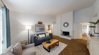 This single-floor residence offers a thoughtfully designed layout with multiple living spaces, bedrooms, and bathrooms. The living room serves as a welcoming focal point, featuring a white-brick fireplace with a raised hearth, soaring angled ceilings that add a sense of volume, and warm carpeted flooring. The open arrangement accommodates comfortable seating and flows naturally into adjoining areas.

The kitchen is bright and functional, featuring rich dark cabinetry, granite-look countertops, an undermount sink, and light hardwood-style flooring. A large sliding door floods the space with natural light and provides room for a casual dining area.

The primary bedroom is generously sized with plush carpeting, a ceiling fan, ample natural light from a large window, and access to a walk-in closet. Its bathroom features a dark wood vanity topped with granite, an undermount sink, and a wide mirror with overhead lighting. A secondary bedroom, well-suited for a child, includes carpeting and a ceiling fan. An additional flexible room functions effectively as a home office, featuring built-in shelving space and soft ambient lighting. A second full bathroom includes a tub-shower combination with textured tile surround and hardwood-style flooring, completing this comfortable and versatile residence.
