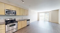 Located at 1450 N Prescott St in Portland, Oregon, this one-bedroom, one-bathroom unit offers a well-designed, single-floor layout with a clean, modern aesthetic throughout. The open-concept kitchen and living area serves as the heart of the space, featuring light maple cabinetry, stainless steel appliances including a range, microwave, dishwasher, and refrigerator, and dark laminate countertops. Track lighting illuminates the kitchen, while wood-style flooring in a cool gray tone extends seamlessly across the entire unit, adding a cohesive, contemporary feel. The living area is bright and airy, benefiting from a large sliding glass door that opens to a private balcony with views of surrounding greenery, allowing generous natural light to fill the room. A wall-mounted mini-split system provides efficient heating and cooling. The bedroom is a comfortable, quiet retreat with a large window overlooking lush outdoor foliage and includes a spacious closet with built-in shelving for ample storage. The bathroom features a light maple vanity with drawers, a large mirror, and warm accent lighting, maintaining the consistent modern design language found throughout the unit. Additional upper cabinetry near the entry provides extra storage convenience.