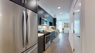 Located at 2315 Valdez St in Oakland, California, this single-floor residence offers a thoughtfully designed layout with a contemporary aesthetic throughout. The galley-style kitchen is a standout feature, outfitted with floor-to-ceiling dark navy cabinetry, stainless steel appliances including a gas range, built-in microwave, and a full-size refrigerator, complemented by a subway tile backsplash and light countertops. Wood-look flooring runs continuously from the kitchen through the hallway, adding warmth and visual cohesion. The living room is bright and welcoming, with large windows that invite an abundance of natural light and provide an open, airy feel. The space comfortably accommodates a full seating arrangement and flows naturally into a dining area. The bedroom features a muted sage green accent wall, warm ambient lighting, and a calm, restful atmosphere. The bathroom is finished with wood-tone flooring, a dark navy vanity with a white countertop, a framed mirror, and a tiled shower-tub combination. Clean white walls throughout the unit enhance the sense of space, while recessed lighting ensures well-distributed illumination in every room. The overall design balances modern finishes with a warm, livable ambiance.