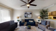 This two-floor residence offers a thoughtfully designed layout with comfortable, functional living spaces throughout. The living room serves as the heart of the home, featuring rich hardwood-style flooring, crown molding, a ceiling fan with light fixture, and a large sliding glass door that floods the space with natural light and provides outdoor views. Two sofas and a central coffee table create an inviting gathering area anchored by a decorative area rug.

The adjacent dining room continues the hardwood-style flooring and is highlighted by an elegant chandelier, crown molding, and a wide window dressed with patterned curtains that allow ample natural light. A marble-top dining table with upholstered navy chairs completes the space.

The kitchen is efficiently designed with dark cabinetry, granite-style countertops, stainless steel appliances including a refrigerator and microwave, and tile flooring, offering everything needed for everyday cooking.

The bedrooms are generously sized, each featuring ceiling fans, hardwood-style flooring, and sliding glass doors or windows with outdoor views. Closet space is provided in each room, ensuring practical storage.

The bathroom is well-finished with a granite vanity, dark wood cabinetry, a tub-shower combination, and tile flooring, connecting conveniently to one of the bedrooms.