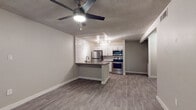 This single-floor residence offers a clean, contemporary aesthetic with consistent wood-look luxury vinyl plank flooring flowing throughout every room. The open-concept living area connects seamlessly to the kitchen via a peninsula counter with a dark quartz-style surface, ideal for casual dining or food preparation. The kitchen is well-appointed with crisp white shaker cabinetry, a bold white subway tile backsplash, stainless steel appliances including a refrigerator, electric range, built-in microwave, and dishwasher, all illuminated by modern track lighting. Ceiling fans with integrated lighting fixtures are present in both the living area and bedroom, promoting airflow and comfort. The bedroom is a calm, neutrally toned space with a window fitted with horizontal blinds, allowing for natural light while maintaining privacy. The bathroom features a floating wood-toned vanity with a clean white integrated sink, a framed mirror, brushed nickel fixtures and towel rings, and a separate water closet for added functionality. The textured ceilings and neutral gray wall tones throughout lend the space a modern, move-in-ready feel. The overall layout, as visible from the dollhouse view, is efficiently arranged and well-proportioned, making the most of the available footprint.