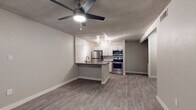 This single-floor residence offers a clean, contemporary aesthetic with consistent wood-look luxury vinyl plank flooring flowing throughout every room. The open-concept living area connects seamlessly to the kitchen via a peninsula counter with a dark quartz-style surface, ideal for casual dining or food preparation. The kitchen is well-appointed with crisp white shaker cabinetry, a bold white subway tile backsplash, stainless steel appliances including a refrigerator, electric range, built-in microwave, and dishwasher, all illuminated by modern track lighting. Ceiling fans with integrated lighting fixtures are present in both the living area and bedroom, promoting airflow and comfort. The bedroom is a calm, neutrally toned space with a window fitted with horizontal blinds, allowing for natural light while maintaining privacy. The bathroom features a floating wood-toned vanity with a clean white integrated sink, a framed mirror, brushed nickel fixtures and towel rings, and a separate water closet for added functionality. The textured ceilings and neutral gray wall tones throughout lend the space a modern, move-in-ready feel. The overall layout, as visible from the dollhouse view, is efficiently arranged and well-proportioned, making the most of the available footprint.