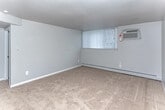 Located at 25231 Rayburn Dr in Warren, Michigan, this single-floor unit offers a straightforward and functional layout across several well-defined living spaces. The main living area is generously sized, finished with neutral beige carpeting, and painted in a soft gray tone throughout. A wall-mounted air conditioning unit and baseboard heating ensure year-round comfort, while a window with a grid-pane design allows natural light to filter in. An additional carpeted room serves as a bedroom, featuring a double-door closet with built-in shelving and hanging rods, providing ample storage. A second carpeted room with a window dressed in vertical blinds and baseboard heating offers flexible use as another bedroom or living space. The kitchen is equipped with warm-toned oak cabinetry, light granite-style countertops, and black appliances including a refrigerator and electric range with overhead ventilation. Light wood-look vinyl flooring extends through the kitchen and into a connected dining or utility area, which also features a ceiling fan. The full bathroom includes a pedestal sink, toilet, and a tub/shower combination with a built-in surround, complemented by wood-look vinyl flooring and a frosted window above the tub for natural light and privacy.