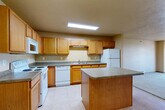 Located at 4105 Montreal St in Bismarck, North Dakota, this one-bedroom, one-bathroom residence offers a practical and well-organized single-floor layout. The kitchen is a standout feature, equipped with warm oak cabinetry providing ample storage, dark laminate countertops, a full suite of white appliances including a range, dishwasher, refrigerator, and microwave, and a central island that adds additional prep space and counter surface. Light tile flooring runs throughout the kitchen and connects seamlessly to the adjacent living area, which is illuminated by a chandelier. The bedroom is a comfortable, carpeted retreat featuring a baseboard heating unit and a window that allows natural light and outdoor views. Neutral, warm-toned walls are consistent throughout the unit, giving the space a cohesive and understated feel. The full bathroom includes tile flooring, a vanity with oak cabinetry and a stone-style countertop, a toilet, and a shower-tub combination. A dedicated in-unit laundry room with tile flooring accommodates a stacked washer and dryer, adding significant everyday convenience. The overall layout, as seen in the dollhouse view, is efficient and well-proportioned, making thoughtful use of the available space.