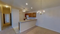 This single-floor residence offers a functional and welcoming layout highlighted by a seamless open-concept design that connects the kitchen and living areas. The kitchen is well-appointed with rich warm-toned wood cabinetry providing ample storage, a white appliance suite including a range and microwave, and a built-in sink. A peninsula-style breakfast bar separates the kitchen from the adjacent living space, offering a casual dining or prep surface while maintaining the open flow of the layout. The living area is finished with plush neutral carpeting, creating a comfortable and inviting atmosphere. Recessed lighting in the kitchen is complemented by a ceiling fan with a light kit, ensuring the space is both bright and well-ventilated. An elegant chandelier with candelabra-style bulbs adds a refined touch to the dining area, enhancing the overall ambiance. Tile flooring in the kitchen transitions cleanly into the carpeted living space, adding a practical distinction between the two zones. A closet near the kitchen provides convenient additional storage. The clean white walls and neutral tones throughout contribute to a bright, airy feel across the entire floor.