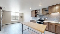 Located at 228 Sheyenne St in West Fargo, North Dakota, this single-floor unit blends contemporary design with rustic character to create a distinctive and functional living space. The open layout is anchored by light-toned hardwood flooring that flows seamlessly throughout, lending a clean and cohesive aesthetic.

A standout feature of the living area is a full-height reclaimed wood accent wall, finished in weathered grays and natural browns, paired with a sliding barn door that adds both visual interest and practical room division. A window with horizontal blinds allows natural light to fill the space.

The kitchen is well-equipped and thoughtfully designed, showcasing rich, warm-toned wood cabinetry, light quartz countertops, and a gray subway tile backsplash. Stainless steel appliances — including a range with an overhead wall-mount range hood, a built-in microwave, and a full-size refrigerator — complete the cooking space. Recessed lighting illuminates the kitchen, and an industrial-style butcher block table serves as a versatile island.

The bathroom offers a polished finish with warm stone-look tile flooring, a wood-toned vanity with an integrated sink, a large mirror, and modern chrome fixtures, providing a spa-like atmosphere. Overall, the space balances urban modern sensibility with warm, textured design elements.