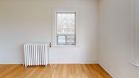 Located at 5 Donlands Ave in Toronto's East End, this one-bedroom, one-bathroom unit offers a functional and efficiently laid-out single-floor residence. The interior is finished with warm hardwood flooring throughout the main living areas and bedroom, lending a clean and inviting ambiance to the space.

The living room is bright and open, benefiting from natural light that enhances the neutral white walls and light wood floors. The bedroom is a comfortable size, featuring a classic cast-iron radiator for heating and a window that looks out to the surrounding neighbourhood, allowing for ample natural light. The hardwood flooring continues here, adding warmth and continuity.

The kitchen is finished with light ceramic tile flooring and includes a window with tree views, providing a pleasant atmosphere for cooking. Cabinetry and a full-size refrigerator complete the practical setup.

The bathroom features full white ceramic tile walls surrounding a soaking tub and shower combination, with matching tile flooring, giving it a clean and classic appearance. A hallway connects all rooms in a straightforward layout, optimizing the use of the available space.

Overall, this unit presents a tidy, no-frills design with consistent finishes, classic architectural details, and a practical configuration suited for comfortable urban living in Toronto.