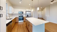 This single-floor home features a thoughtfully designed open-concept layout that connects the kitchen and living room into one cohesive, light-filled space. The living area is anchored by a large bank of floor-to-ceiling windows that frame expansive outdoor views, flooding the space with natural light and complementing the warm wood-look hard flooring found throughout the main areas.

The kitchen is well-equipped with stainless steel appliances, a mix of white upper cabinetry and warm wood lower cabinets, a subway tile backsplash, quartz countertops, and a central island with pendant lighting above — ideal for both meal prep and casual dining.

The three bedrooms are carpeted for comfort, each featuring ceiling fans and windows that bring in natural light. The primary bedroom connects to a private en-suite bathroom with warm wood vanity cabinetry and black hardware accents, as well as a spacious walk-in closet outfitted with extensive built-in shelving and hanging rods. Secondary bedrooms are served by additional closets with double-door access and dual hanging rods.

The three bathrooms maintain a clean, modern aesthetic with wood-toned vanities and wood-look flooring. A dedicated laundry room accommodates a full-size washer and dryer with overhead shelving for added convenience.