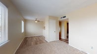 Located at 7694 Alameda Ave in El Paso, Texas, this single-story unit offers a practical and straightforward layout across several connected rooms. The living area features a combination of wood-look hard flooring and neutral-toned carpet, with a ceiling fan overhead and a textured ceiling throughout. Painted cinder block walls in a warm beige tone add a distinctive architectural element visible in multiple rooms, contributing to the unit's sturdy construction. A built-in shelf cutout provides a subtle design detail within the living space, which connects to additional rooms via an open hallway.

The bedrooms are carpeted and receive natural light through windows fitted with horizontal blinds. Each room includes a ceiling-mounted light fixture and is finished with the same warm, neutral palette seen throughout the unit.

The kitchen is equipped with a gas range, an overhead exhaust hood, light-colored countertops, dark cabinetry, and a decorative linear mosaic tile backsplash in muted gray and brown tones. The bathroom includes a single-sink vanity with a mirrored cabinet, a toilet, and a soaking tub with a tiled surround in earthy tones. Hard flooring is present in the bathroom, complementing the overall design. Overhead HVAC vents are present throughout, ensuring climate control across the space.