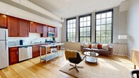 Located at 655 Eden Park Dr in Cincinnati, Ohio, this one-bedroom, one-bathroom residence showcases a compelling blend of industrial loft character and modern finishes. The open-plan living and kitchen area is immediately striking, featuring soaring ceilings with exposed structural elements, light-toned hardwood floors, and oversized multi-pane industrial windows that flood the space with abundant natural light and offer leafy outdoor views. The kitchen is outfitted with rich dark walnut cabinetry, granite countertops, a classic subway tile backsplash, and a full suite of stainless steel appliances, including a refrigerator, dishwasher, microwave, and range. The expansive living and dining area benefits from the generous ceiling height and sunlight, creating an open, airy ambiance ideal for both relaxing and entertaining. The bedroom is a serene retreat with plush carpeting, elevated ceilings with industrial detailing, large windows that connect visually to the living area, and a dedicated closet. The bathroom is finished with marble-look tile flooring, a rich wood vanity with granite countertop, a framed mirror, and a glass-enclosed walk-in shower with subway tile surround. Throughout the residence, the thoughtful combination of industrial architecture and refined finishes creates a distinctive and comfortable urban living environment.