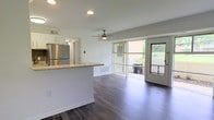 This single-floor space at 620 101 offers a clean, modern layout centered around an open-concept living and kitchen area. Dark hardwood flooring runs throughout, providing a rich contrast against the crisp white walls and bright recessed lighting overhead. A ceiling fan adds both style and comfort to the main living area, which flows seamlessly toward large sliding glass doors and a secondary glass door that open to an outdoor area, flooding the interior with natural light and providing easy access to the greenery beyond.

The kitchen is defined by a peninsula-style counter finished with granite-look stone, offering additional prep and seating space. White cabinetry lines the kitchen walls, complemented by a stainless steel refrigerator that adds a sleek, contemporary touch. The open sightlines between the kitchen and living area make the space feel expansive and connected.

The overall ambiance is light, airy, and functional, with a neutral palette that creates a welcoming environment. The combination of natural light from the glass doors, modern finishes, and an open floor plan makes this a well-appointed, move-in-ready space suited for a variety of uses.