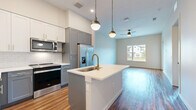 This well-appointed 2-bedroom, 2-bathroom residence in Austin, TX offers a thoughtfully designed single-floor layout that maximizes comfort and functionality. The open-concept kitchen and living area serves as the heart of the home, anchored by a central island with a white quartz countertop, an undermount sink, and a brushed gold faucet. Stylish pendant lights hang overhead, complementing the two-tone cabinetry — white upper cabinets with a subway tile backsplash and slate gray lower cabinets with gold hardware. Stainless steel appliances, including a French door refrigerator, electric range, and built-in microwave, complete the modern kitchen. Rich hardwood flooring runs throughout the entire space, adding warmth and continuity. The open living area benefits from natural light through a large window and features a ceiling fan for year-round comfort. Both bedrooms are well-sized, with the primary bedroom offering additional space and access to a walk-in closet fitted with wrap-around shelving and hanging rods. The bathrooms are clean and modern, with one featuring a glass-enclosed walk-in shower, a vanity with a white countertop, and continued hardwood flooring. The secondary bedroom enjoys a bright window with neighborhood views.