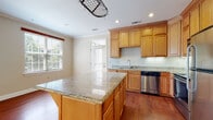 This single-floor residence offers a thoughtfully designed layout that balances functionality and comfort throughout. The kitchen is a standout feature, showcasing warm honey-toned cabinetry that extends to the ceiling, polished granite countertops, and a full suite of stainless steel appliances including a refrigerator, range, microwave, and dishwasher. Rich hardwood flooring anchors the kitchen and flows seamlessly into the adjoining dining area, while a large central island with a granite surface provides additional prep space and is topped with a decorative pot rack. The open living area is bright and welcoming, featuring a brick fireplace, built-in shelving, crown molding, and a ceiling fan. Large windows and glass doors invite an abundance of natural light and provide access to an outdoor balcony. The bedrooms are comfortably carpeted with crown molding details, ceiling fans, and generous closet space, including a walk-in closet in the primary bedroom. The bathrooms are finished with tile flooring and warm wood vanities with granite counters. The primary bath includes a walk-in glass shower, while a secondary bathroom offers a tub-shower combination. Overall, the space presents a clean, classic aesthetic with consistent finishes throughout.
