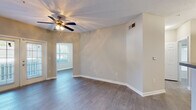 This single-story space offers a thoughtfully organized layout with distinct living, kitchen, and bedroom areas connected by consistent design choices throughout. The main living area features wood-style flooring, neutral beige walls, a textured ceiling, and a ceiling fan with a light fixture. Multiple windows allow natural light to fill the space, with views of the surrounding greenery. An adjoining area with additional windows extends the living space and provides flexibility in use.

The galley-style kitchen is lined with white cabinetry, granite-look countertops, and black appliances including a refrigerator, range, and dishwasher. Light wood-style flooring continues through the kitchen, which also provides access to a utility or storage area housing the electrical panel.

The bedroom features plush carpeting, a ceiling fan, and vaulted-style ceilings that add a sense of openness. A walk-in closet with built-in shelving and rods offers practical storage, while a connected bathroom includes a white tiled tub-shower combination equipped with safety grab bars and wood-style flooring. Additional rooms display light flooring and generous window placement, maintaining a bright and airy atmosphere throughout the space.