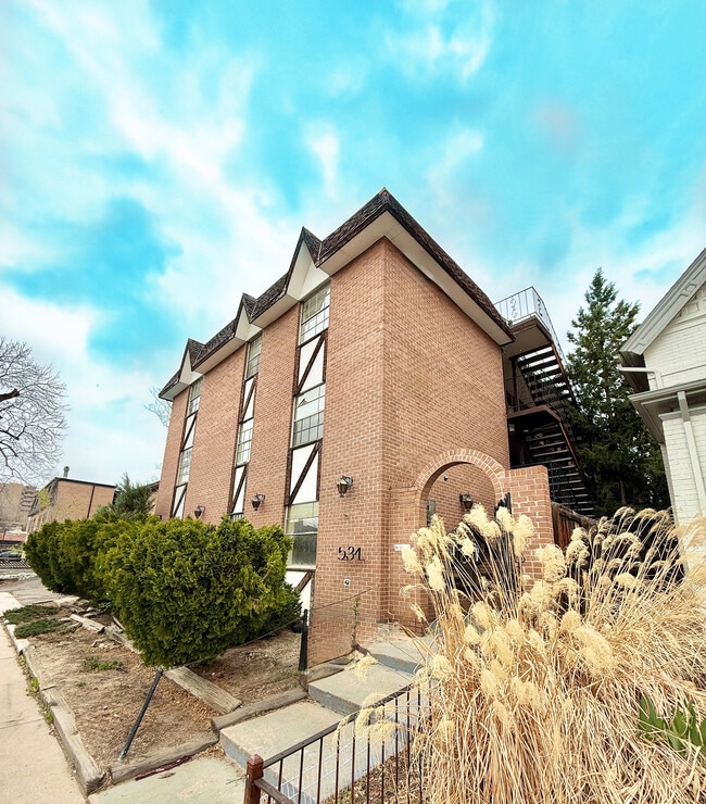 Charming brick apartment building with unique architectural design and lush landscaping under a vibrant blue sky. - Washington Plaza