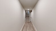This three-story home offers a thoughtfully organized layout across its three levels. The ground floor features a garage with a concrete floor, interior staircase access, and utility connections including a water heater. A clean, light-filled hallway with light wood-style flooring connects the lower level seamlessly to the main living areas above.

The main floor serves as the heart of the home, combining the kitchen and living room in an open, airy arrangement. The kitchen is outfitted with white shaker-style cabinetry, white quartz countertops, a subway tile backsplash, stainless steel appliances including a range and dishwasher, and light hardwood-style flooring. Two windows allow natural light to brighten the space. The adjacent living room features the same flooring, a ceiling fan, and a staircase leading to the upper level.

The upper floor hosts the five bedrooms, three full bathrooms, a closet, and a dedicated laundry room. Bedrooms are carpeted and benefit from natural light through large windows with exterior views. The bathrooms are finished with light wood-style flooring, neutral walls, and brushed nickel fixtures — one featuring a tub-shower combo and another offering a walk-in shower with sliding glass doors and a single vanity. The laundry room includes a full-size washer and dryer with overhead shelving.