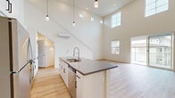 Located at 200 E 31st St in National City, CA, this thoughtfully designed two-story home offers a bright, modern aesthetic across two well-proportioned floors. The main level is anchored by a dramatic open-concept kitchen and living area distinguished by soaring double-height ceilings that flood the space with natural light from strategically placed clerestory and standard windows. The kitchen features a large central island with a dark quartz countertop, undermount sink, stainless steel appliances, crisp white cabinetry with matte black hardware, a subway tile backsplash, and elegant pendant lighting overhead. Light-toned hardwood flooring runs throughout both levels, enhancing the clean, contemporary feel. A staircase leads to the upper floor, where a bright hallway connects to the primary bedroom, a dedicated closet, and two well-appointed bathrooms. Each bathroom includes a white vanity with a quartz countertop, tub-shower combination, and wood-look flooring. The spacious bedroom benefits from a wall-mounted mini-split system and a large window framing neighborhood views. A private balcony accessible from the main level offers open-air outdoor space with views of the surrounding National City neighborhood, completing this well-appointed home.