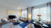 This single-floor residence presents a thoughtfully designed layout that balances open communal spaces with private quarters. The living area serves as the focal point, featuring warm hardwood-style flooring, a ceiling fan, and large windows dressed with horizontal blinds and sheer curtains that draw in generous natural light. A contemporary media console anchors one wall beneath bold abstract artwork, while a plush sofa, layered area rug, and round coffee table complete the comfortable seating arrangement. The dining area flows seamlessly from the living space, accommodating a round table and modern chairs.

The kitchen is efficiently designed with wood-grain cabinetry extending to the upper walls, a white countertop, subway tile backsplash, and a full suite of stainless steel appliances including a dishwasher, range, microwave, and refrigerator.

The bedroom offers a serene retreat with elevated ceilings, soft neutral tones, and a spacious closet with built-in shelving. Artwork above the headboard and warm bedside lighting contribute to a calm, polished atmosphere.

The bathroom features a clean, minimal aesthetic with a tub-shower combination, white tile surround, a single vanity with wood-toned cabinetry, and hardwood-style flooring throughout.