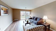 This single-floor residence offers a functional and comfortable layout across a thoughtfully arranged floor plan. The living room serves as the heart of the space, featuring warm hardwood-style flooring, neutral taupe walls, and a large sliding glass door that floods the room with natural light and provides direct access to an outdoor patio with views of the surrounding greenery.

The galley-style kitchen is well-equipped with ample warm-toned wood cabinetry on both sides, a double sink, a full-size refrigerator, and a coil-top range. A pendant light fixture illuminates the space, and the kitchen flows seamlessly into a dedicated dining area, which features hardwood-style flooring and a chandelier overhead — ideal for everyday meals or entertaining.

Both bedrooms are generously sized, carpeted for comfort, and finished with neutral gray-toned walls. Each room benefits from natural light through windows, and the primary bedroom includes a closet with additional built-in shelving. The two bathrooms are finished with classic white subway-style tile wainscoting, mosaic tile flooring, warm wood vanity cabinetry with white countertops, and overhead storage. One bathroom includes a glass-enclosed shower stall, adding a refined touch to the overall design.