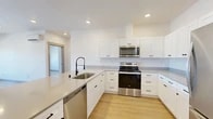 Located at 102 E Farwell in Spokane, WA, this well-appointed one-bedroom, one-bathroom unit offers a clean, modern aesthetic across a thoughtfully designed single-floor layout. The open-concept kitchen and living area forms the heart of the space, highlighted by crisp white shaker cabinetry, light quartz countertops, and a central island with an undermount sink and a sleek matte black faucet. Stainless steel appliances — including a range, over-the-range microwave, dishwasher, and refrigerator — complete the kitchen. Light wood-look flooring runs throughout, complementing the bright white walls and recessed lighting that create a clean, airy atmosphere. The living area is spacious and open, benefiting from large windows that invite natural light and provide outdoor views. A wall-mounted mini-split unit ensures year-round comfort in both the living area and bedroom. The bedroom is a comfortable, well-proportioned retreat featuring its own mini-split unit and access to a generously sized walk-in closet with wire shelving. The bathroom is finished with a grey shaker vanity, a round mirror with modern lighting, and a bifold closet door for additional storage. Light wood flooring continues here, maintaining a cohesive look throughout the entire unit.