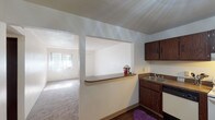 This single-floor unit at 3400 Evergreen Lane in Saint Louis, Missouri, offers a straightforward and functional layout designed to maximize everyday comfort. The living area is generously proportioned, featuring neutral-toned carpet, textured ceilings, and walls bathed in natural light streaming through vertical-blind-covered windows and a sliding glass door that opens to an outdoor patio. This connection to the outdoors enhances the sense of openness throughout the living space.

The kitchen is positioned adjacent to the living area and is connected via a pass-through window with a countertop ledge, creating an open, communicative feel between the two spaces. The kitchen itself is equipped with dark wood cabinetry offering ample storage, a double sink, an electric range, a dishwasher, and a full-size refrigerator, all set atop durable wood-style flooring.

The bedrooms are carpeted and well-lit, each featuring windows with vertical blinds. One bedroom includes a closet, providing practical storage. The bathroom is cleanly appointed with a single vanity sink set in a laminate countertop, a mirrored medicine cabinet with overhead lighting, and a tub-shower combination. Overall, the unit presents a clean, practical living environment.