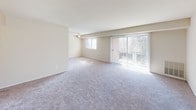 This single-story residence offers a practical and comfortable layout thoughtfully arranged across several rooms. The living area is generously sized, finished with plush wall-to-wall carpeting and bathed in natural light streaming through a large sliding glass door dressed with vertical blinds, which provides outdoor views of surrounding greenery. A ceiling fan adds functionality overhead, and an additional window further brightens the space.

The kitchen is efficiently designed with warm wood-toned cabinetry providing ample storage, dark countertops, and light wood-look flooring. It is equipped with a gas range, refrigerator, and a sink set beneath upper cabinets, making the most of its compact footprint.

The bedrooms are carpeted and neutrally finished, each featuring windows fitted with horizontal blinds that allow for natural light and privacy. One bedroom includes a dedicated walk-in closet with built-in shelving, while another features its own closet with rod storage. The two bathrooms differ in configuration: one includes a corner-entry glass-enclosed shower with light wood-look flooring, while the other offers a full tub-shower combination with white tile surround. Throughout, the unit maintains a clean, neutral palette.