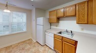 This single-floor residence offers a straightforward and functional layout designed for comfortable everyday living. The kitchen is well-equipped with warm oak cabinetry providing ample storage, light-toned countertops, a coil-burner electric range, dishwasher, refrigerator, and a single-basin sink. Tile-style flooring runs throughout the kitchen, adding durability to the space.

The living area is generously sized, featuring neutral carpet and a tiled entryway that transitions smoothly between spaces. Natural light filters in through blinds-covered windows, offering views of the surrounding exterior. The bedrooms are carpeted and maintain a clean, neutral palette, each featuring closets with shelving and hanging rods for organized storage.

Two bathrooms serve the residence, each outfitted with a tub-shower combination featuring chrome fixtures and clean white surrounds. A dedicated laundry area houses a full-sized washer and dryer with an overhead wire shelving rack, adding notable convenience. Throughout the home, white walls, consistent trim work, and practical finishes create a cohesive and move-in-ready environment.