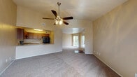 This single-floor residence is designed with an open, functional layout that connects the main living areas seamlessly. The spacious living room is a standout feature, showcasing vaulted ceilings accented by a ceiling fan with integrated lighting, neutral-toned walls, and plush wall-to-wall carpeting. A sliding glass door leads to a private balcony, filling the room with natural light and providing convenient outdoor access.

The kitchen is accessible via a pass-through counter that opens directly to the living area, promoting an inclusive, connected feel. It features rich, medium-toned wood cabinetry, speckled countertops, and black appliances including a range with overhead ventilation and a refrigerator.

The bedrooms are carpeted and finished with neutral walls, each benefiting from window blinds that allow for natural light control. Closet access is present in the bedrooms, providing practical storage solutions.

The bathroom is well-appointed with warm wood-toned cabinetry, a speckled countertop with an undermount sink, wood-look flooring, and a tiled tub-shower combination featuring a decorative tile accent border. A second vanity area with mirrored medicine cabinets connects to the bathroom, offering added convenience and storage throughout the unit.