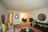 Located at 100 Radcliff Lane in Newport News, Virginia, this single-floor residence offers a well-organized layout designed for comfortable everyday living. The open living room is generously proportioned, featuring soft carpeting, neutral-toned walls, and large windows dressed with sheer curtains that allow natural light to fill the space. The room provides ample room for a variety of furniture arrangements.

The galley-style kitchen is efficiently designed with white cabinetry lining both sides, dark countertops, a gas range, dishwasher, and a window above the sink area that brings in natural light. The tile flooring adds a practical, easy-to-maintain surface throughout the cooking space.

Multiple bedrooms are present throughout the unit, each carpeted and finished with neutral walls. The primary bedroom is notably spacious and features dual closets, offering generous storage. Additional bedrooms are well-sized, with windows framing views of surrounding greenery, and provide comfortable, private retreats.

The bathroom is clean and simply appointed, featuring a white vanity with a single-basin sink, a mirror, and standard fixtures. The overall design of the home emphasizes functionality and comfort, with consistent neutral finishes and soft carpeting creating a cohesive, livable atmosphere throughout.