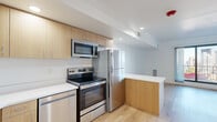 Located at 5 Grandview Ave in Pittsburgh's scenic Mount Washington neighborhood, this single-floor unit showcases a clean, modern design with an open, airy layout. Light hardwood flooring runs throughout, lending warmth and continuity to the space.

The kitchen is a standout feature, outfitted with light wood cabinetry, white countertops, and a full suite of stainless steel appliances including an electric range, over-the-range microwave, refrigerator, and dishwasher. A peninsula counter extends the workspace and provides a natural transition into the open living area, which benefits from large sliding glass doors that invite natural light and offer outdoor views.

A secondary kitchen or kitchenette area is also present, similarly appointed with light wood cabinetry, white countertops, a stainless steel sink, and matching appliances, suggesting flexible use of the space. The bedroom features expansive black-framed floor-to-ceiling windows that frame views of the surrounding architecture and flood the room with natural light.

The bathroom is finished with elegant marble-look tile flooring, a gray vanity with a mirrored medicine cabinet, and crisp white walls, creating a clean and polished atmosphere. Recessed lighting and a neutral white palette throughout contribute to the bright, contemporary feel of the overall space.