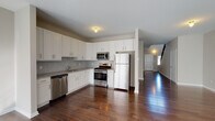 This two-story home offers a thoughtfully designed layout with consistent finishes throughout. The main level features rich, dark hardwood flooring that flows seamlessly from the open-concept kitchen and dining area into the spacious living room. The kitchen is well-equipped with white shaker-style cabinetry, granite countertops, a classic subway tile backsplash, and a full suite of stainless steel appliances including a gas range, built-in microwave, refrigerator, and dishwasher. The adjacent living room is bright and airy, benefiting from abundant natural light through large windows with vertical blinds, recessed lighting, and a sleek fireplace with a marble surround as a focal point. A wide hallway on the main level connects the living spaces and leads to a staircase featuring elegant dark wood balusters with carpeted treads. The upper floor continues the hardwood flooring and includes carpeted bedrooms, one of which offers direct access to an en-suite bathroom with a glass-enclosed shower. Additional bathrooms feature granite-topped vanities, tile flooring, and a full tub-shower combination. The home presents a clean, modern aesthetic with neutral tones throughout, offering a polished and move-in-ready environment.