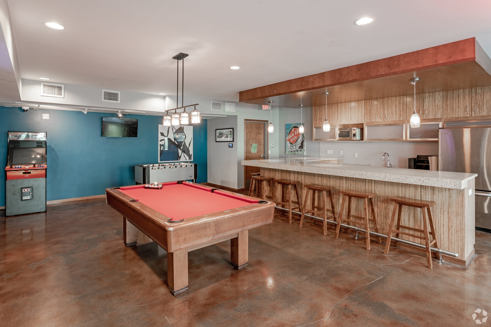 Community lounge with pool table, foosball, arcade game, and a full-service bar with stools.