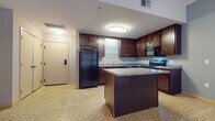 This single-floor unit offers a thoughtfully designed layout centered around a fully equipped kitchen. The kitchen is a standout feature, showcasing rich dark wood cabinetry with sleek hardware, granite-style countertops, and a suite of black appliances including a refrigerator, electric range, built-in microwave, and dishwasher. A central kitchen island provides additional prep and serving space, while under-cabinet lighting adds a warm, functional ambiance. Open glass shelving accents the cabinetry, adding a modern touch. The kitchen flows naturally into the adjoining living areas, creating an open and connected feel throughout the space.

The bathroom is clean and functional, featuring a dark wood vanity with a white countertop, a large mirror, and a full tub-shower combination. Neutral gray walls and terrazzo flooring carry the cohesive aesthetic found throughout the unit.

A separate room offers a window with views of a neighboring building, allowing natural light to filter in through slatted blinds. This versatile space is well-suited for use as a bedroom or home office.

Terrazzo flooring runs consistently throughout the entire unit, lending a polished, durable, and visually distinctive character to every room. The overall design is modern and functional, with a neutral color palette that provides a clean, move-in-ready foundation.