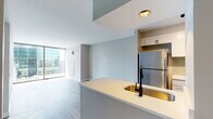 Located at 210 W Lake St in Chicago's vibrant Loop neighborhood, this single-floor unit showcases a contemporary design with clean lines and a neutral color palette throughout. The open-concept layout connects the kitchen and living area seamlessly, creating a cohesive and functional living space.

The kitchen is equipped with stainless steel appliances, including a full-size refrigerator, range, and microwave. White cabinetry provides ample storage, while the kitchen island features a light countertop and a distinctive gold-toned undermount sink paired with a matte black faucet, adding a refined contrast to the otherwise understated design. Light tile flooring grounds the kitchen area.

The living space is defined by its expansive floor-to-ceiling sliding glass doors that open to a private balcony, offering direct views of Chicago's iconic downtown skyline. Light wood-tone flooring runs throughout the main living areas, contributing to the unit's bright and airy atmosphere.

The bedroom also benefits from floor-to-ceiling glass doors leading to outdoor access, further maximizing natural light and skyline views. The bathroom is finished with neutral tile flooring, a white vanity with cabinet storage, and matte black hardware and fixtures, maintaining the consistent modern aesthetic found throughout the unit.
