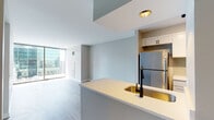 Located at 210 W Lake St in Chicago's vibrant Loop neighborhood, this single-floor unit showcases a contemporary design with clean lines and a neutral color palette throughout. The open-concept layout connects the kitchen and living area seamlessly, creating a cohesive and functional living space.

The kitchen is equipped with stainless steel appliances, including a full-size refrigerator, range, and microwave. White cabinetry provides ample storage, while the kitchen island features a light countertop and a distinctive gold-toned undermount sink paired with a matte black faucet, adding a refined contrast to the otherwise understated design. Light tile flooring grounds the kitchen area.

The living space is defined by its expansive floor-to-ceiling sliding glass doors that open to a private balcony, offering direct views of Chicago's iconic downtown skyline. Light wood-tone flooring runs throughout the main living areas, contributing to the unit's bright and airy atmosphere.

The bedroom also benefits from floor-to-ceiling glass doors leading to outdoor access, further maximizing natural light and skyline views. The bathroom is finished with neutral tile flooring, a white vanity with cabinet storage, and matte black hardware and fixtures, maintaining the consistent modern aesthetic found throughout the unit.