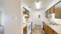 This single-story home offers three bedrooms, two bathrooms, a kitchen, a laundry area, and a connecting hallway, all laid out on one level. The living area features neutral-toned carpet, a textured ceiling, and a large window that allows natural light to fill the room, creating a bright and open atmosphere. A hallway connects the living space to the private bedrooms and bathrooms, maintaining a clear and functional flow throughout the home. The bedrooms continue the carpeted flooring and feature ceiling fans with lighting, along with windows that bring in additional natural light. The galley-style kitchen is equipped with wood-toned cabinetry, light laminate countertops, a white electric range, a full-size refrigerator, a dishwasher, and a double-basin stainless steel sink. Stone-look tile flooring runs through the kitchen, bathrooms, and laundry area, providing a durable and cohesive aesthetic across the wet zones. The bathrooms include wood-toned vanity cabinetry and matching tile flooring. The dedicated laundry area includes dryer hookups and an overhead shelf for added storage. Throughout the home, neutral wall tones and consistent finishes create a clean, understated interior.